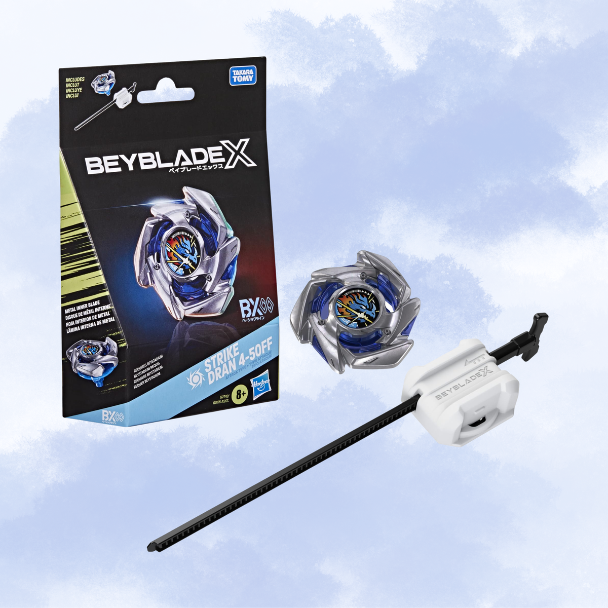 Beyblade X Metal Burst toy set showing the retail box, a silver and blue spinning top, and a black string launcher against a light blue cloudy background. Visible brands include Beyblade X, Hasbro, and Bandai.