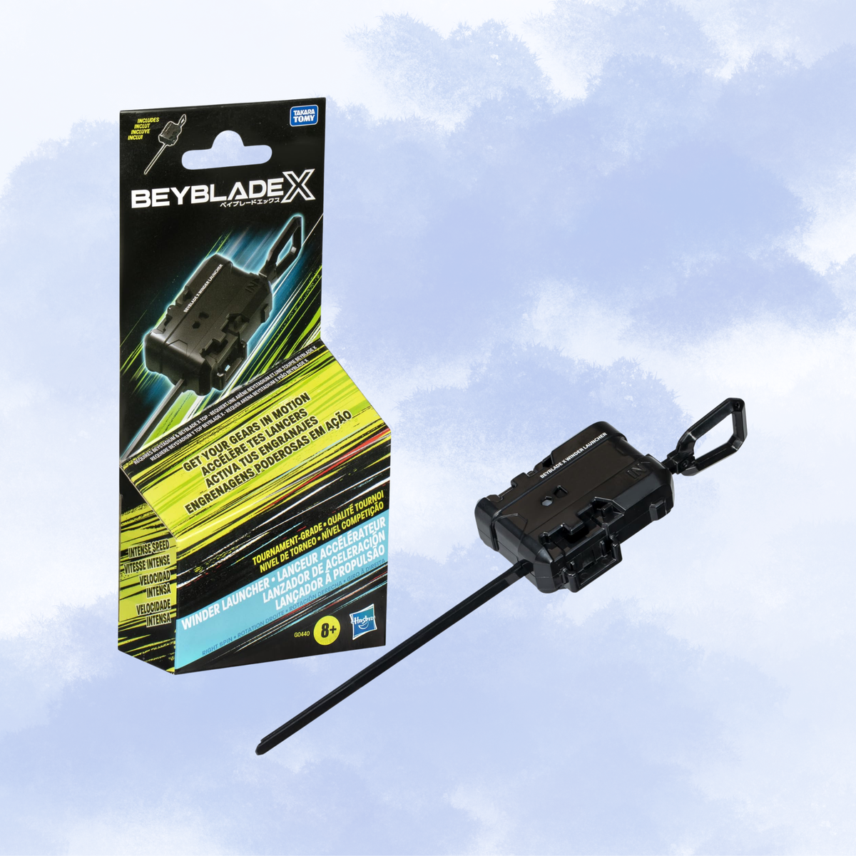 Beyblade X winder launcher shown next to its retail packaging against a light blue cloudy background.